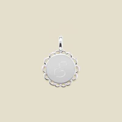 Silver pendant with engraved letter 'E' on a beige background