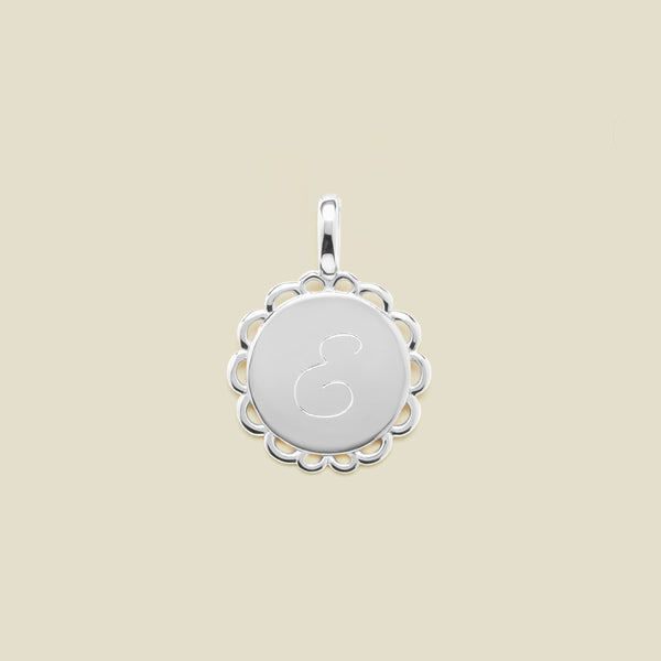 Silver pendant with engraved letter 'E' on a beige background
