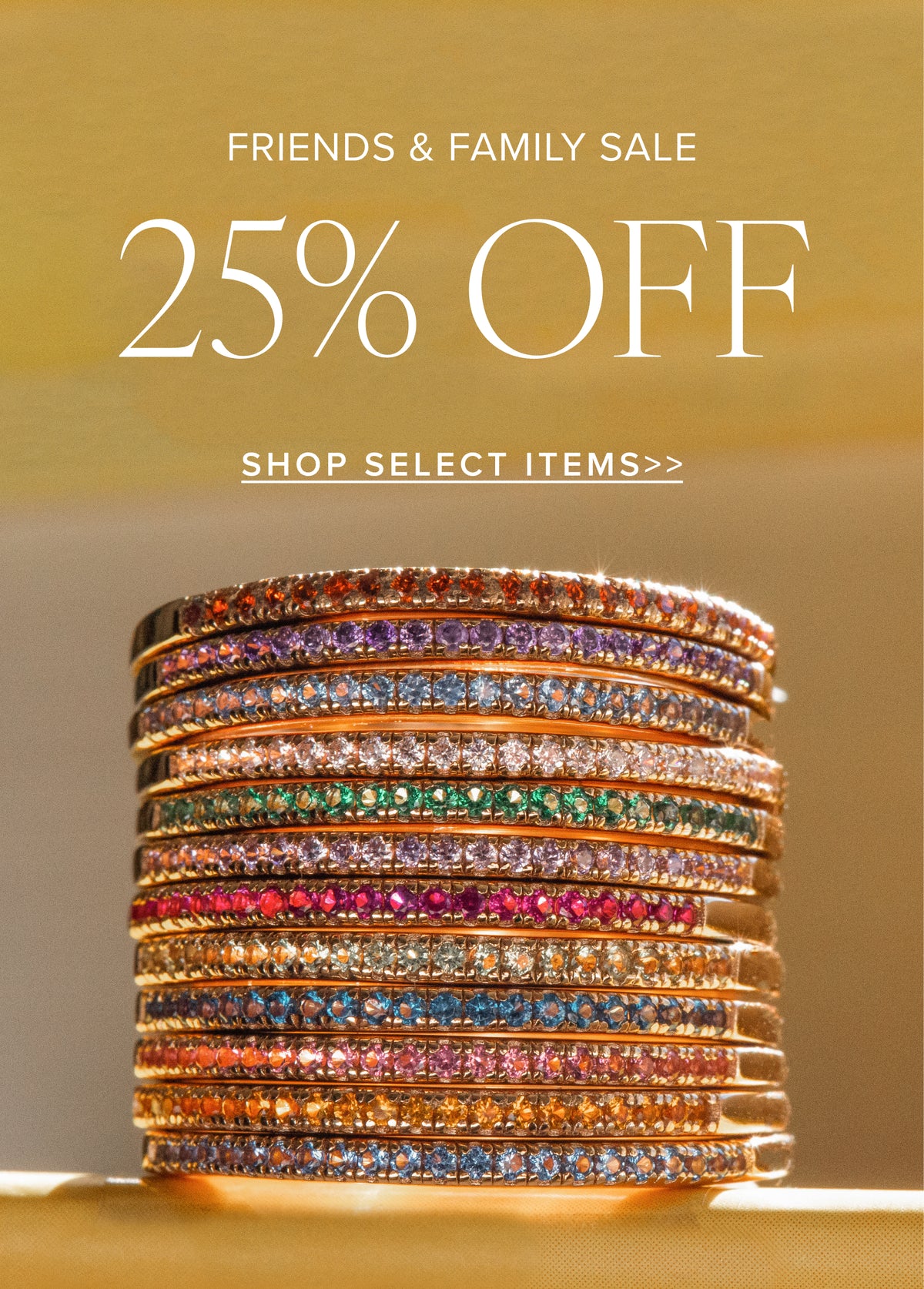A promotional sale graphic with the text 'FRIENDS & FAMILY SALE 25% OFF SHOP SELECT ITEMS>>' above a stack of gold rings set with many colored gemstones on a warm beige background.