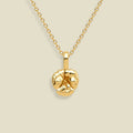 A gold chain necklace with a textured, violet flower pendant, displayed against a solid light beige background.