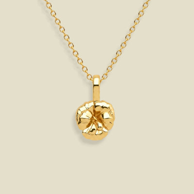 A gold chain necklace with a textured, violet flower pendant, displayed against a solid light beige background.