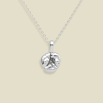 A silver pendant necklace featuring a textured, violet flower pendant on a delicate link chain, set against a solid light beige background.