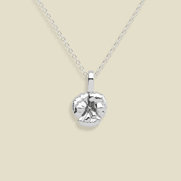 A silver pendant necklace featuring a textured, violet flower pendant on a delicate link chain, set against a solid light beige background.