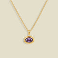 A gold chain necklace with a pendant featuring a bezel-set oval purple CZ gemstone and a small clear accent stone above it, shown on a light beige background.