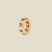 A gold ring charm with multiple bezel set square-cut purple gemstones set side by side to create the band, shown on a solid beige background.
