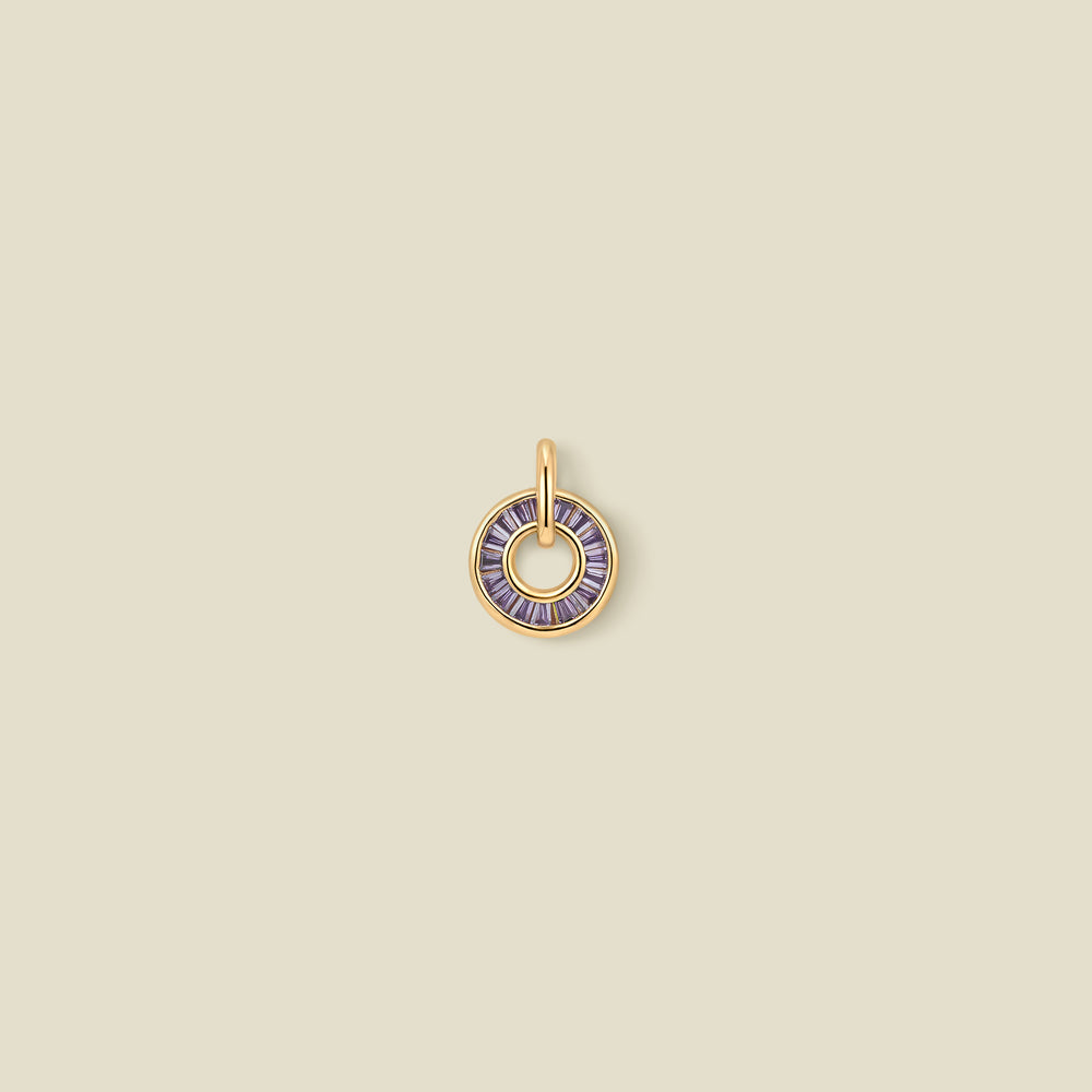 A circular gold pendant featuring purple baguette-cut stones around a hollow center, displayed against a solid light beige background.