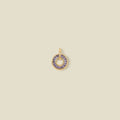 A circular gold pendant featuring purple baguette-cut stones around a hollow center, displayed against a solid light beige background.