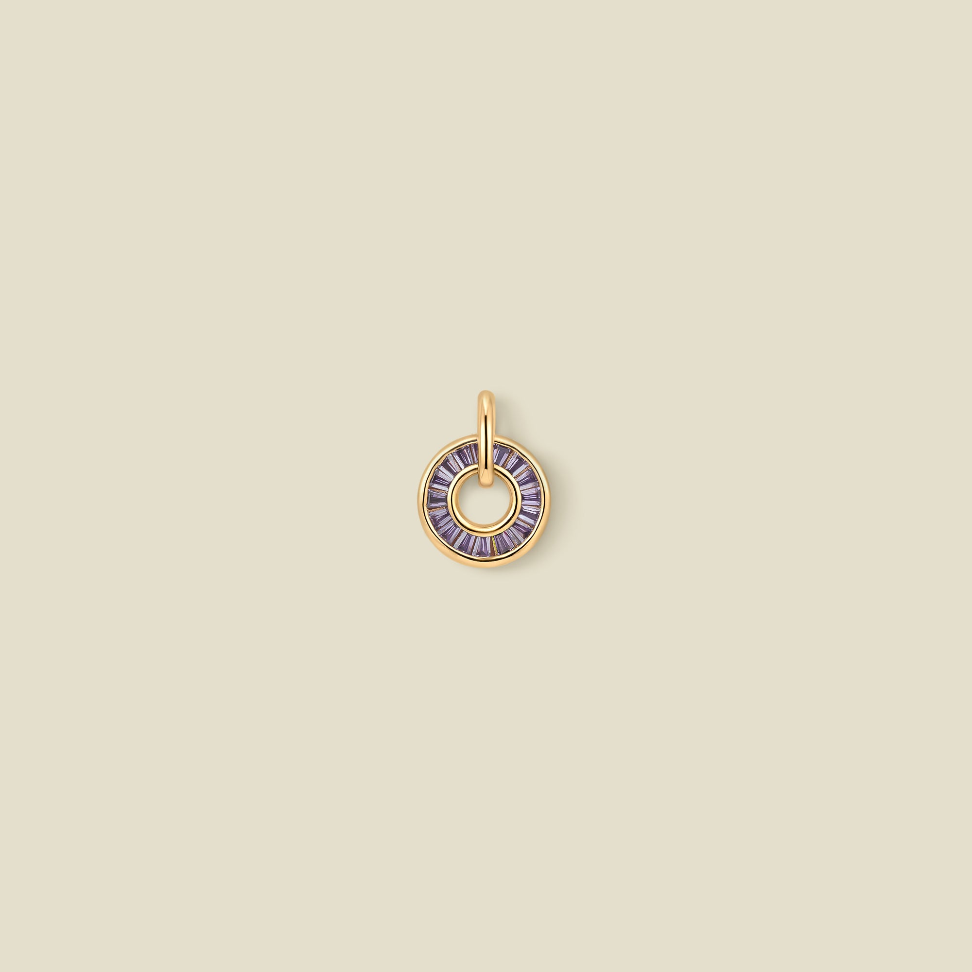 A circular gold pendant featuring purple baguette-cut stones around a hollow center, displayed against a solid light beige background.
