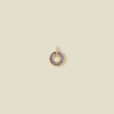 A circular gold pendant featuring purple baguette-cut stones around a hollow center, displayed against a solid light beige background.