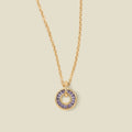 A gold chain necklace with a circular pendant featuring purple baguette-cut stones around a hollow center, displayed against a solid light beige background.
