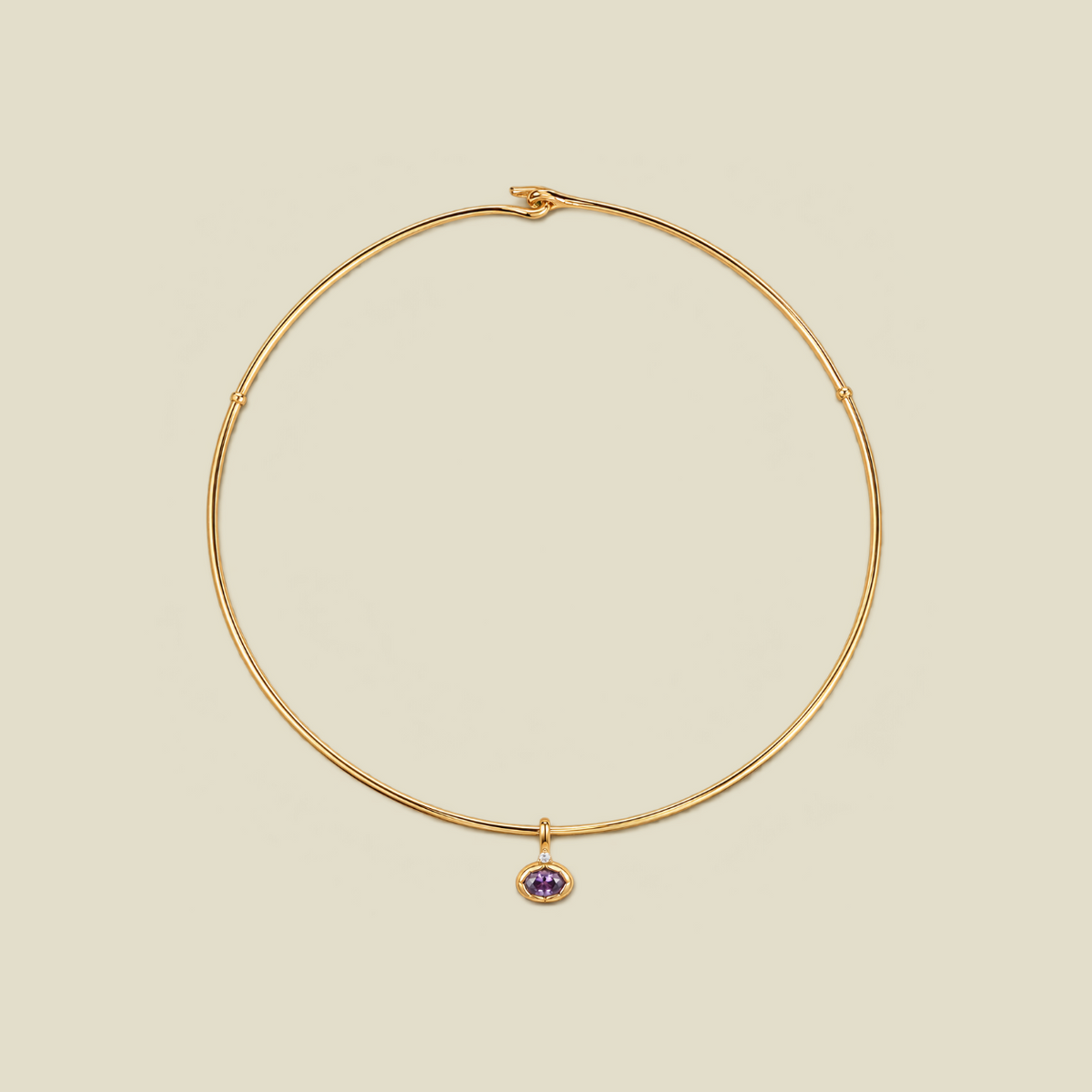 A thin gold wire necklace with a small purple oval gemstone charm, displayed on a solid beige background.