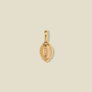 A polished gold football-shaped pendant with detailed lacing, centered on a solid light beige background.