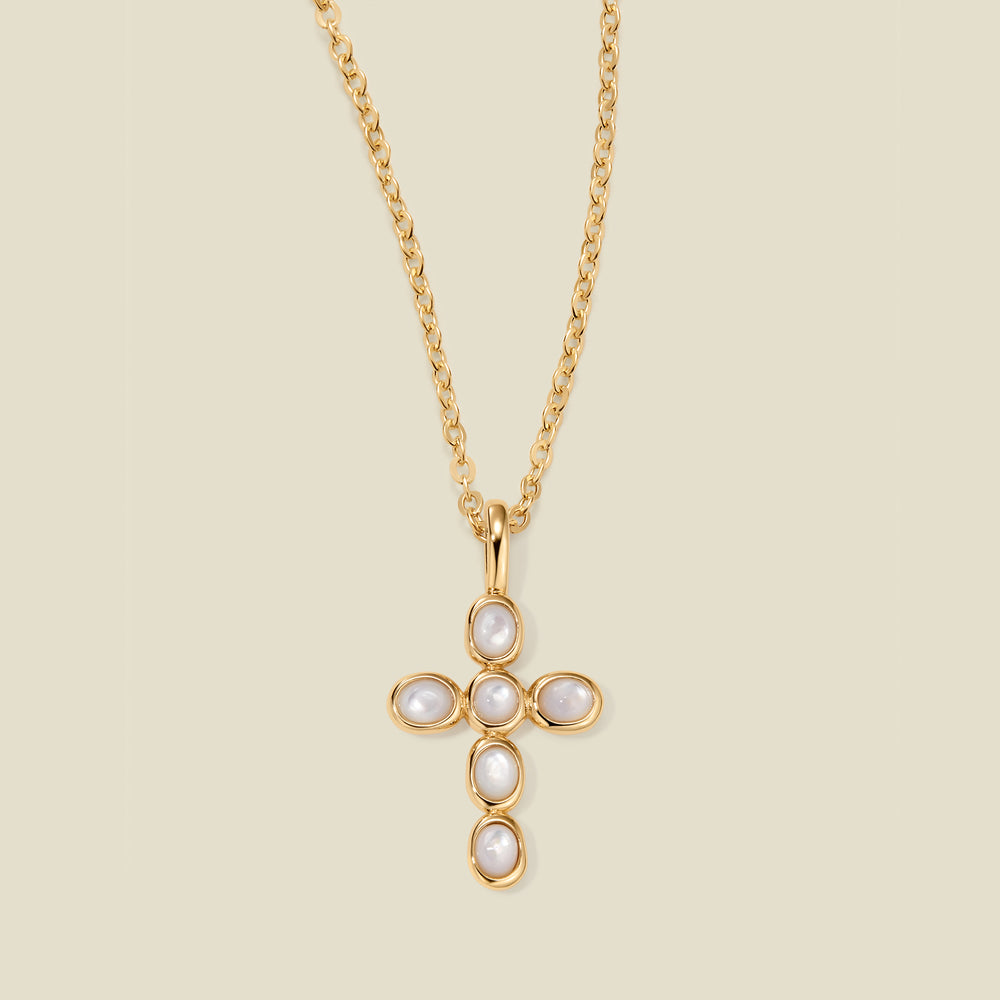 Gold necklace with a cross pendant made of bezel-set pearl stones against a neutral background.