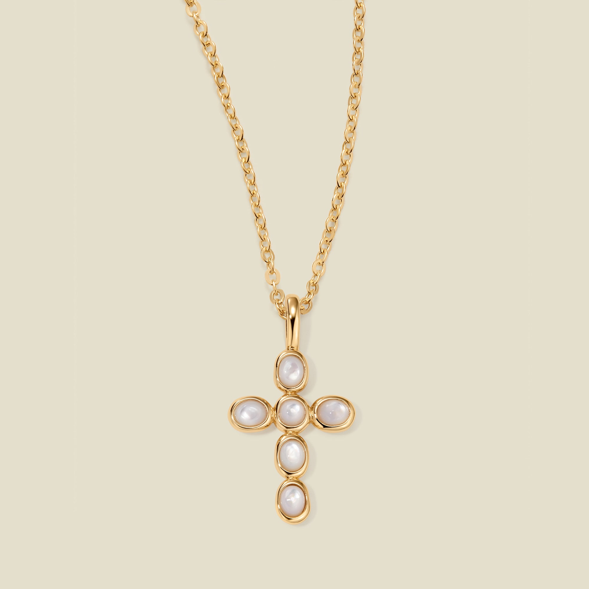 Gold necklace with a cross pendant made of bezel-set pearl stones against a neutral background.
