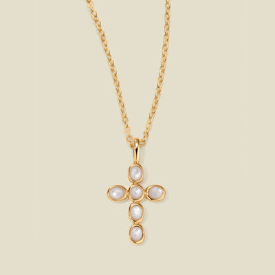 Gold necklace with a cross pendant made of bezel-set pearl stones against a neutral background.