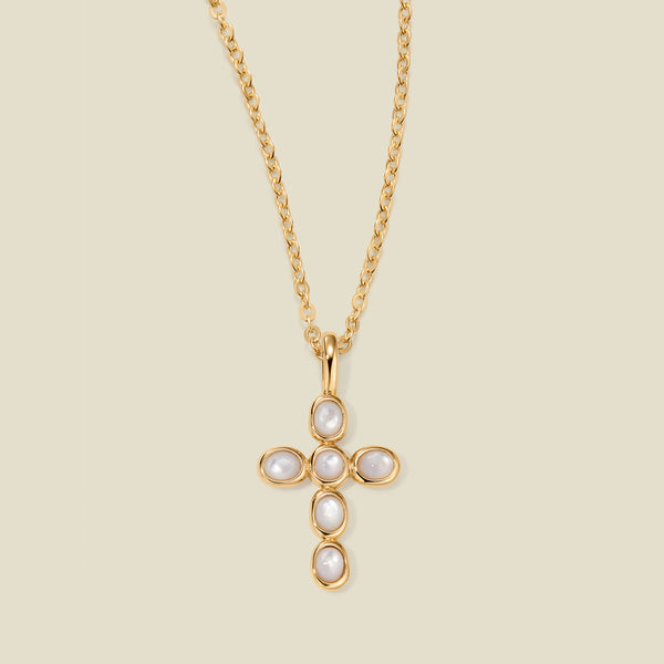 Gold necklace with a cross pendant made of bezel-set pearl stones against a neutral background.