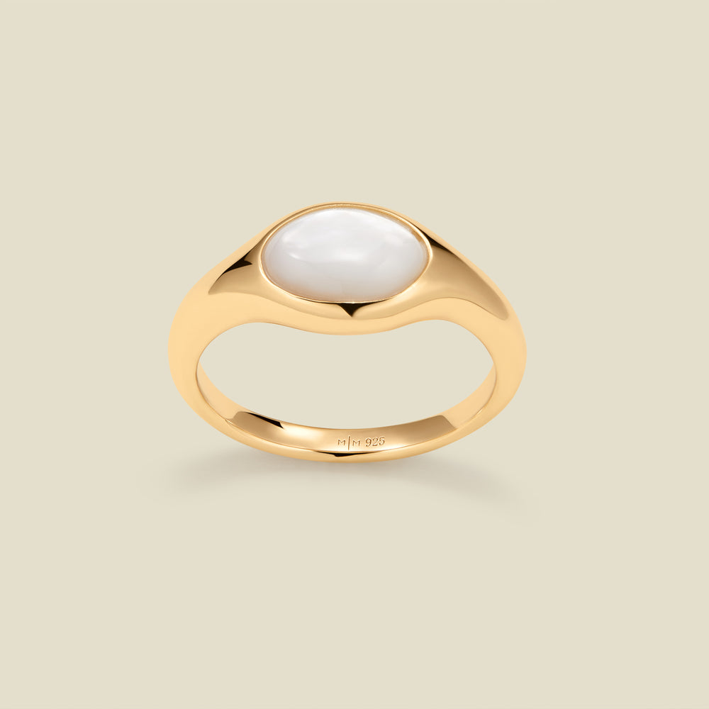 Gold ring with a bezel-set pearl stone against a neutral background.
