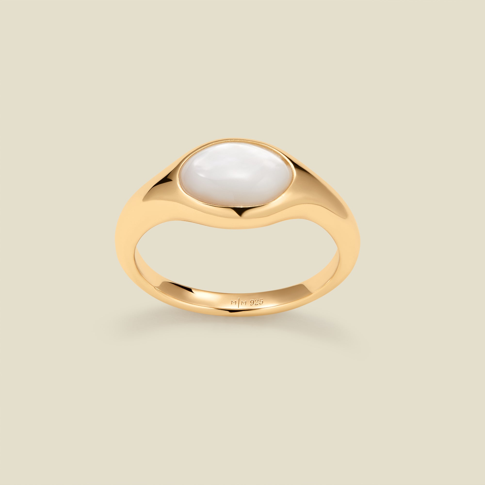 Gold ring with a bezel-set pearl stone against a neutral background.