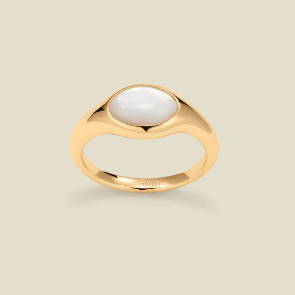 Gold ring with a bezel-set pearl stone against a neutral background.