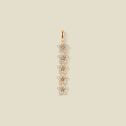 A gold pendant charm with five stars stacked vertically with clear stones, set against a solid beige background.