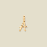 A polished gold initial pendant charm shaped like the letter 'A' in a cursive script, centered on a solid light beige background.