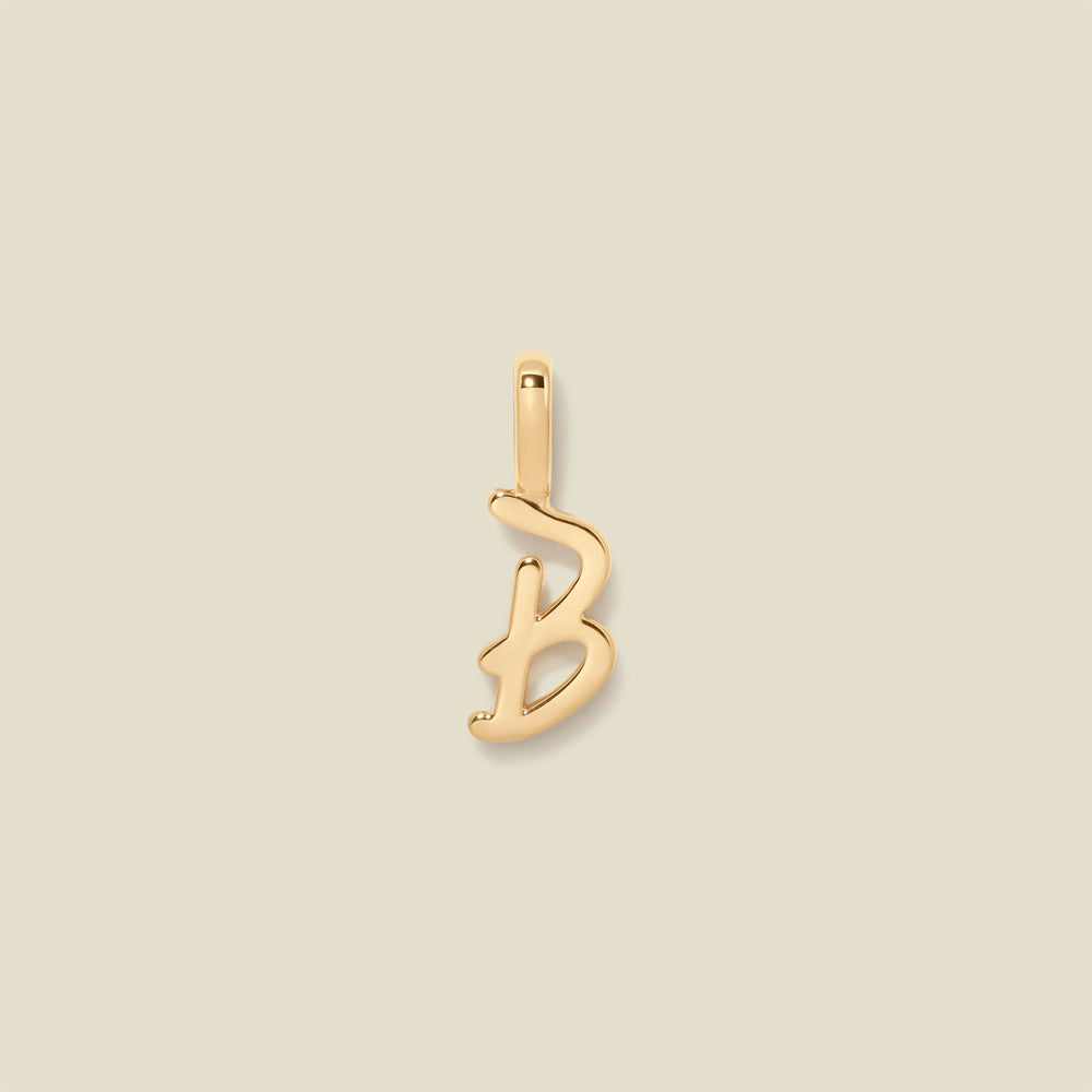 Gold initial "b" charm on a beige background