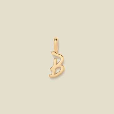 Gold initial "b" charm on a beige background