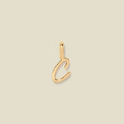 A polished gold initial pendant charm shaped like the letter 'C' in a cursive script, centered on a solid light beige background.