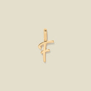 A polished gold initial pendant charm shaped like the letter 'F' in a cursive script, centered on a solid light beige background.