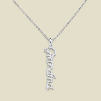 A silver script nameplate necklace spelling 'Grandma'  hanging vertically on a delicate silver chain, presented on a solid light beige background.