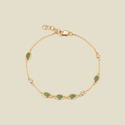 Gold bracelet with bezel-set green and clear stones against a neutral background.