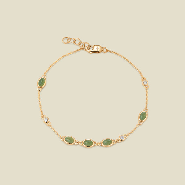 Gold bracelet with bezel-set green and clear stones against a neutral background.