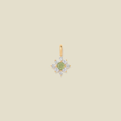 Gold charm with prong-set green and clear stones against a neutral background.