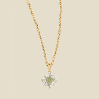 Gold chain with a green prong-set pendant against a neutral backdrop.