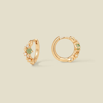 Gold hoop earrings with prong-set green and clear stones against a neutral background.