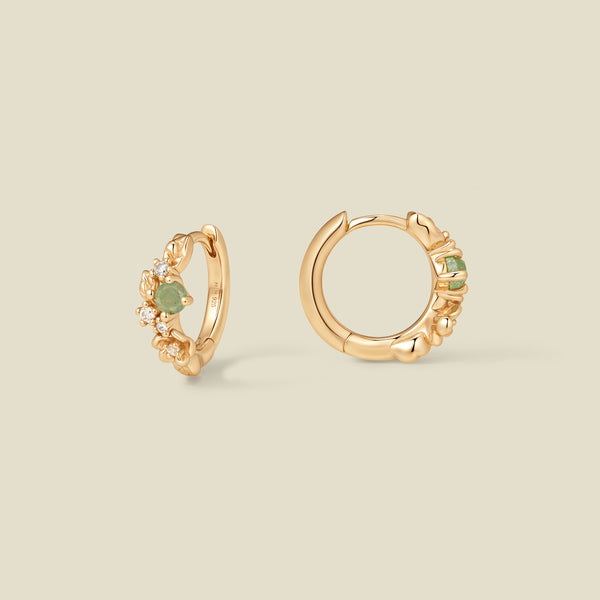 Gold hoop earrings with prong-set green and clear stones against a neutral background.
