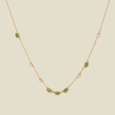Gold necklace with green and clear bezel-set stones against a neutral backdrop.
