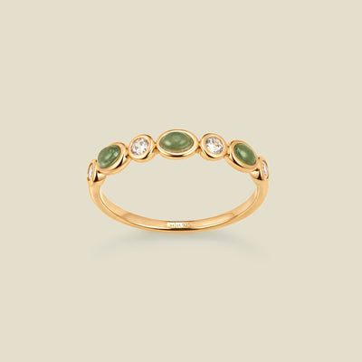 Gold ring with bezel-set green and clear stones against a neutral background.