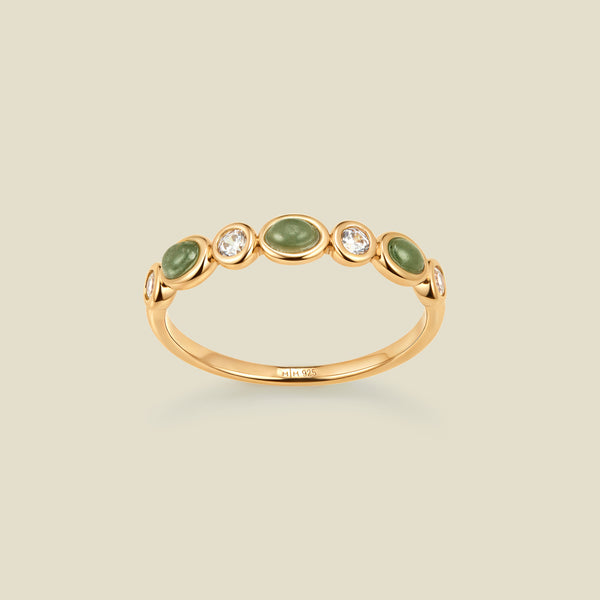 Gold ring with bezel-set green and clear stones against a neutral background.
