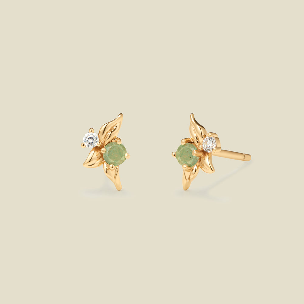 Gold stud earrings with prong set green and clear stones against a neutral backdrop.