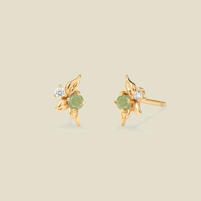 Gold stud earrings with prong set green and clear stones against a neutral backdrop.