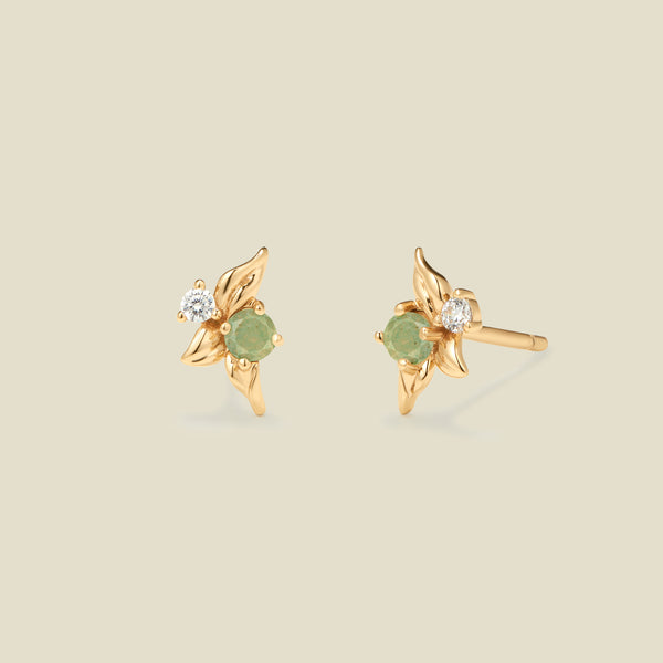 Gold stud earrings with prong set green and clear stones against a neutral backdrop.