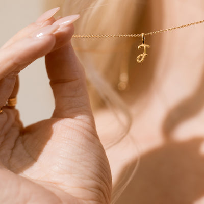 Close-up of woman holding a gold chain with a pendant letter J.