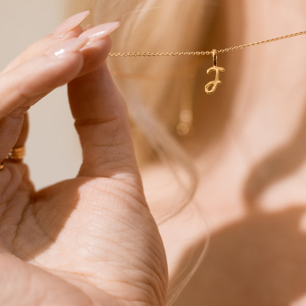 Close-up of woman holding a gold chain with a pendant letter J.