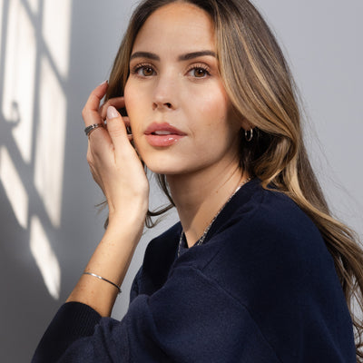 A woman with long light brown hair wearing a dark navy blue knit top, posing in soft window light with shadows on a gray wall.