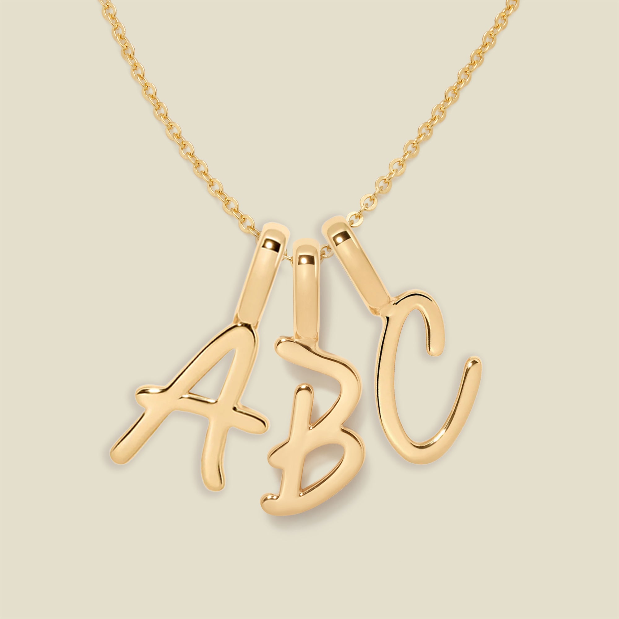 Gold necklace with 'ABC' initial charms on a beige background