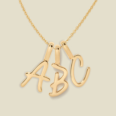Gold necklace with 'ABC' initial charms on a beige background