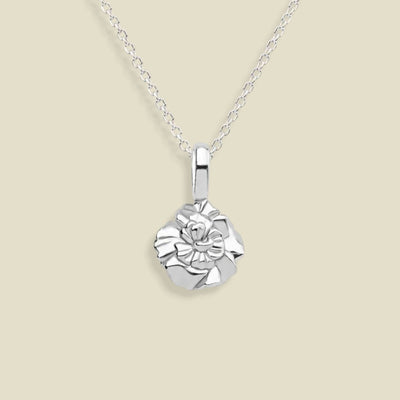 A silver necklace with a small, textured carnation flower pendant, displayed against a solid light beige background.