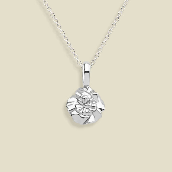 A silver necklace with a small, textured carnation flower pendant, displayed against a solid light beige background.