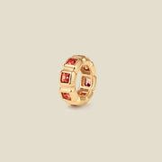 A gold ring charm with multiple bezel set square-cut red gemstones set side by side to create the band, shown on a solid beige background.
